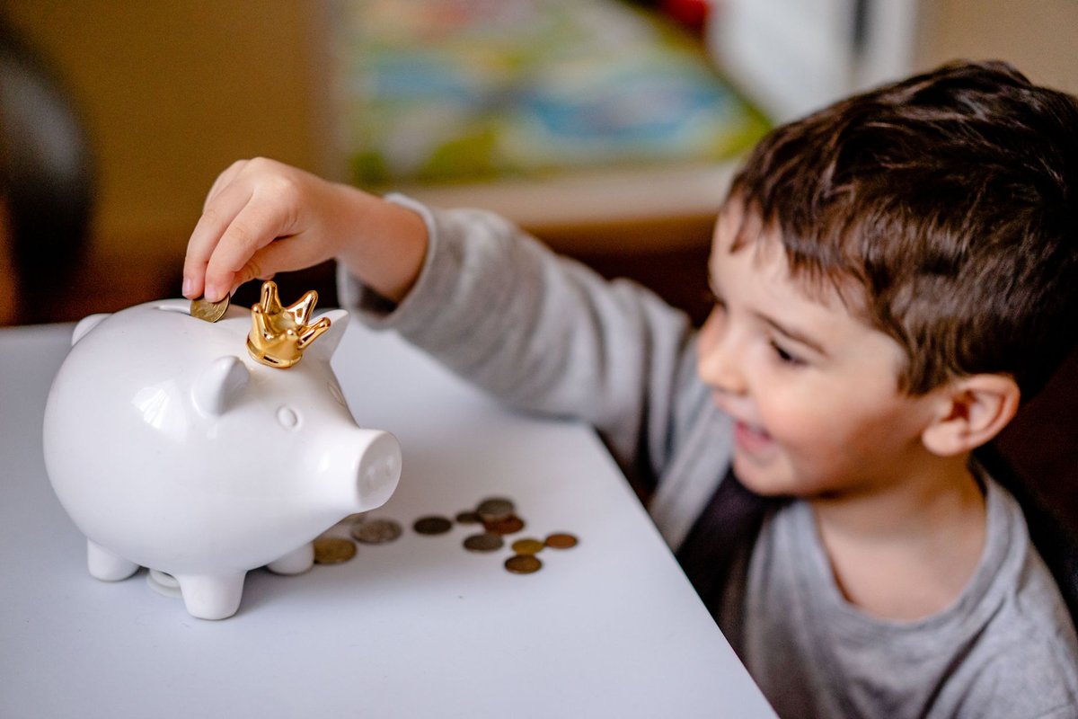 豚の貯金箱にコインを入れる幼い子ども