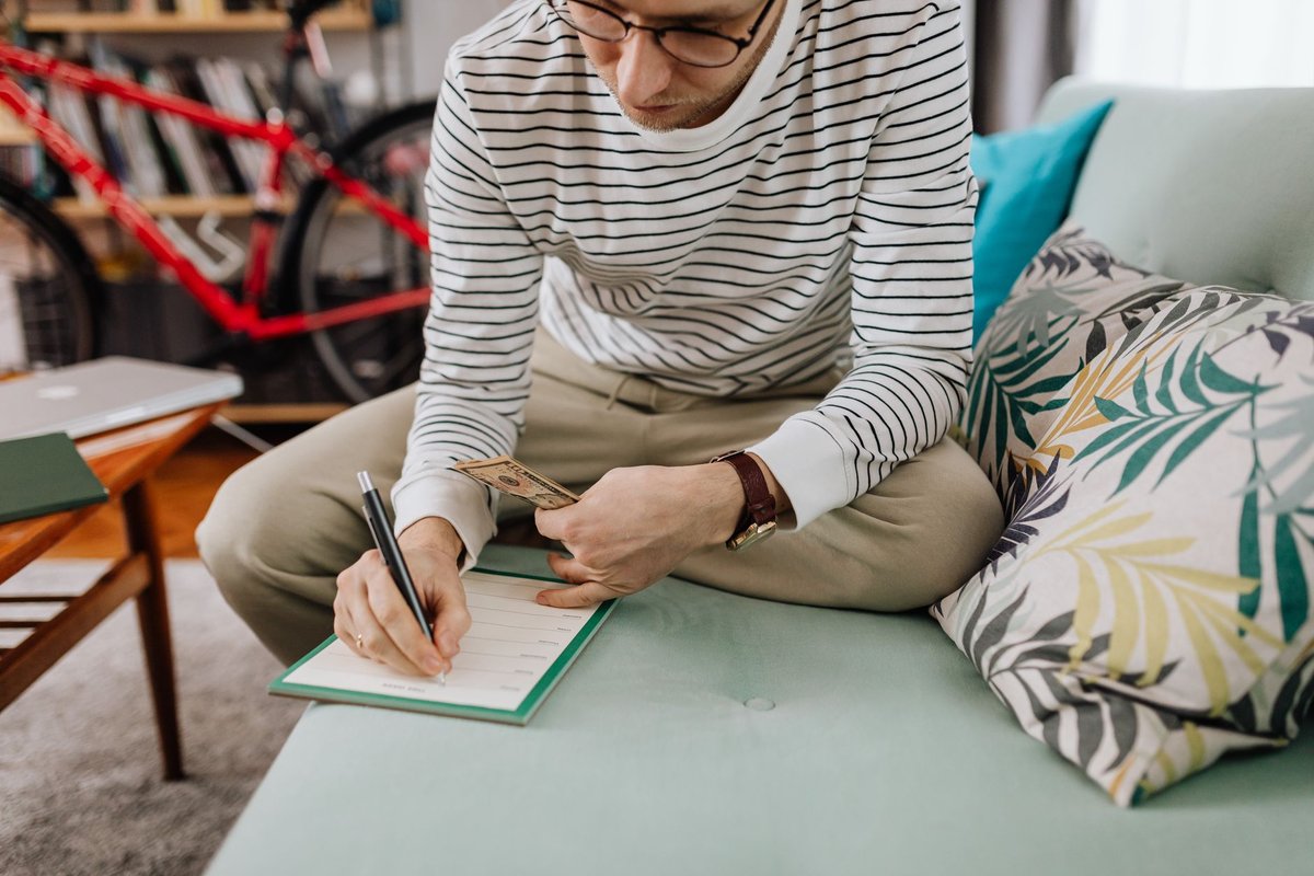 ソファで手帳に家計を書き留める男性